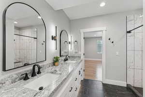 Bathroom with double vanity, a marble finish shower, dark marble finish flooring, and recessed lighting