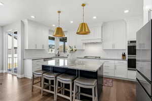 Dual tone kitchen with light stone counters, a kitchen breakfast bar, a center island, stainless steel appliances, and two tone cabinets