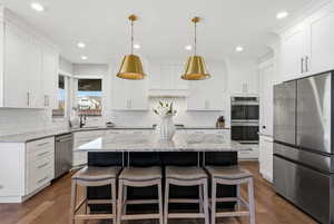 Kitchen featuring stainless steel appliances, a breakfast bar area, light stone counters, and white cabinets