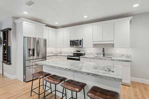 Kitchen with stainless steel appliances, light wood finished floors, a kitchen bar, light stone countertops, and white cabinets