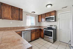 Kitchen featuring stainless steel appliances, tile countertops, a textured ceiling, and light tile patterned flooring