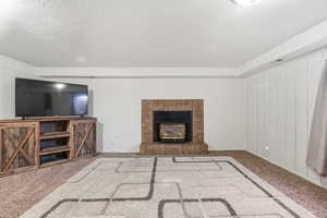 Unfurnished living room with carpet floors, wood walls, a textured ceiling, and a fireplace