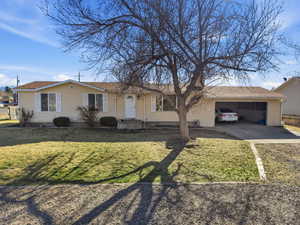 Ranch-style home with concrete driveway, a garage, roof with shingles, and a front yard