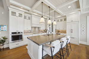 Kitchen featuring glass fronted cabinets, a breakfast bar, oven, hanging light fixtures, and a center island with sink