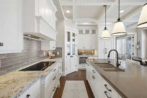 Kitchen with white cabinets, light stone counters, dark wood-style floors, black electric stovetop, and pendant lighting