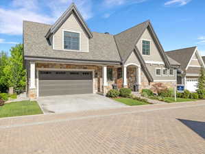 Craftsman-style exterior featuring stone and shake siding, an integrated two-car garage, a covered entry with columns, and a landscaped front yard