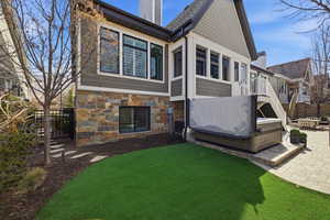 Back of property with a hot tub, a chimney, a patio, stone siding, and a wooden deck