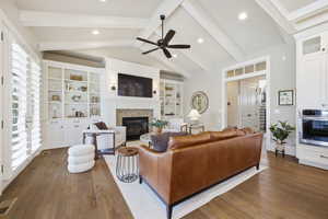 Living room featuring dark wood-style flooring, recessed lighting, ceiling fan, a glass covered fireplace, and beam ceiling