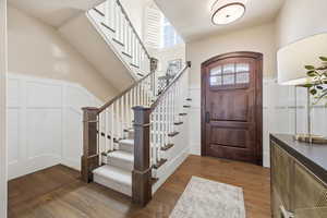 Entrance foyer featuring dark wood-style floors, a decorative wall, wainscoting, and vaulted ceiling