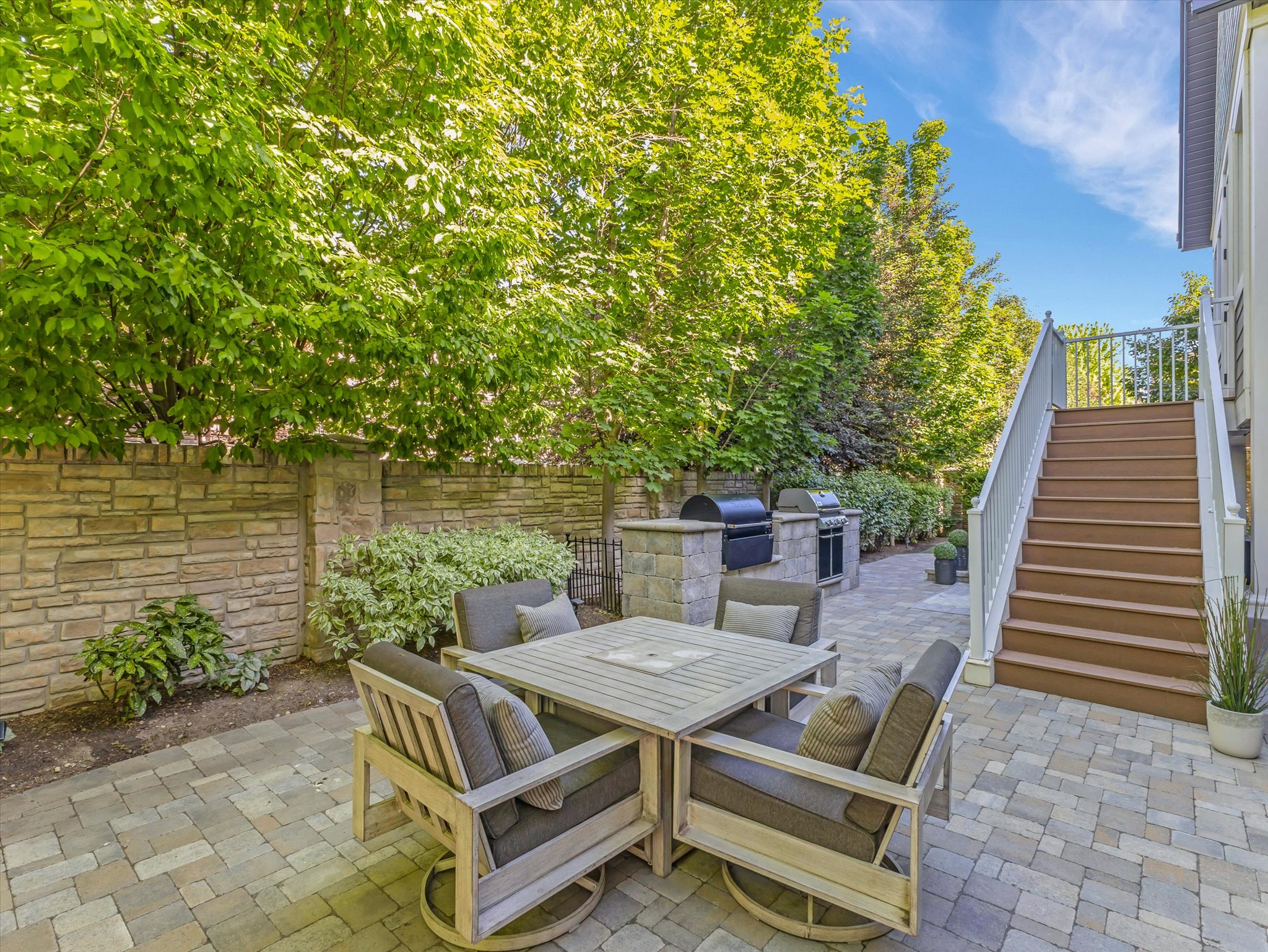 Paver patio featuring a stone veneer privacy wall and built-in outdoor kitchen with grill stations