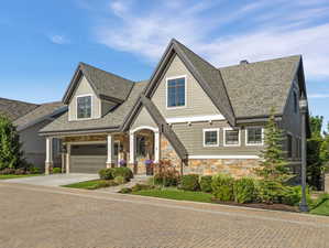 Gabled residence featuring stone and siding exterior, a paver driveway, and an integrated garage