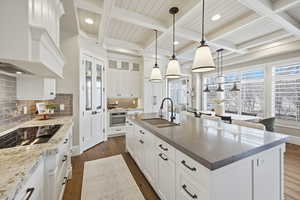 Kitchen with white cabinets, dark wood finished floors, coffered ceiling, tasteful backsplash, and a center island with sink