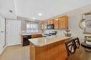 Kitchen featuring light countertops, a peninsula, black appliances, and light tile patterned floors