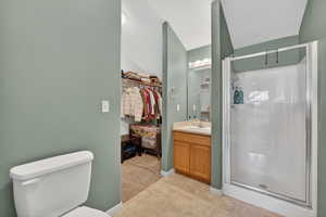 Full bathroom featuring vanity, a walk in closet, a shower stall, light tile patterned floors, and light carpet
