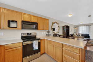 Kitchen featuring stainless steel electric stove, a peninsula, open floor plan, black microwave, and light countertops