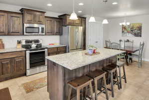 Kitchen featuring dark wood finish cabinets, stainless steel appliances, a breakfast bar, light stone counters, and a center island