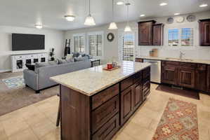 Kitchen with dark wood finish cabinetry, open floor plan, a center island, and light stone countertops