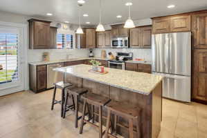 Kitchen with stainless steel appliances, a breakfast bar area, light stone counters, pendant lighting, and a kitchen island