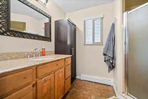 Bathroom with vanity, a baseboard heating unit, a textured ceiling, and a shower stall