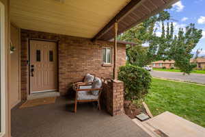 Doorway to property featuring a yard, brick siding, and a porch