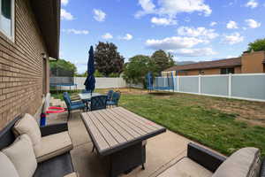 Fenced backyard with a trampoline, a patio area, and an outdoor living / dining area