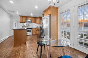 Kitchen featuring a kitchen island, dark stone counters, stainless steel appliances, wood finish cabinets, and recessed lighting