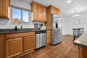 Kitchen featuring stainless steel appliances, dark stone counters, suspended lighting, wood finish cabinetry, and dark tile patterned flooring