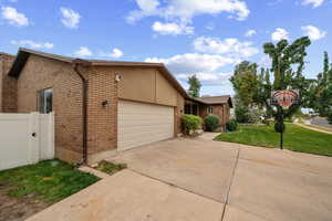 View of property exterior featuring brick siding, a garage, concrete driveway, and a lawn