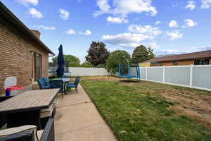 Fenced backyard featuring a trampoline, outdoor dining area, and a patio