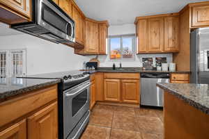 Kitchen featuring stainless steel appliances, dark stone countertops, and wood finish cabinetry