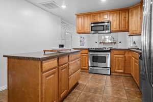Kitchen with dark stone counters, stainless steel appliances, dark tile patterned flooring, and wood finish cabinets