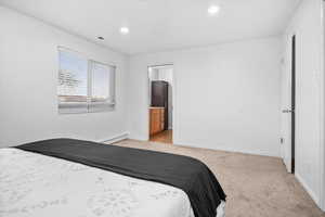 Bedroom with light colored carpet, a baseboard heating unit, recessed lighting, and connected bathroom