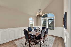 Dining room with vaulted ceiling, hanging lights, light wood-type flooring, and a wainscoted wall
