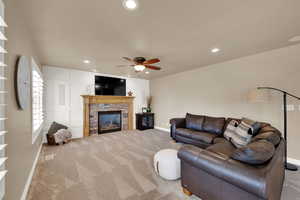 Carpeted living area with a stone fireplace, ceiling fan, and recessed lighting