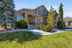 View of front of house featuring stone siding, a front lawn, and stucco siding