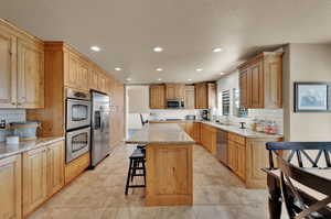 Kitchen featuring recessed lighting, a center island, stainless steel appliances, light stone counters, and a breakfast bar area