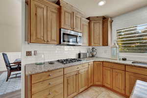 Kitchen with light stone countertops, stainless steel appliances, decorative backsplash, recessed lighting, and a textured ceiling