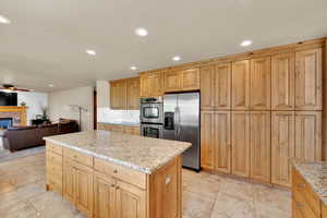 Kitchen featuring stainless steel appliances, open floor plan, a kitchen island, a fireplace, and light stone countertops