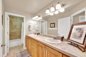 Full bath with double vanity, light tile patterned flooring, and shower / bath combo
