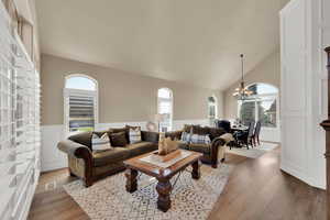 Living area featuring vaulted ceiling, a chandelier, wood finished floors, wainscoting, and a decorative wall
