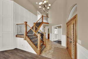 Foyer entrance with a decorative wall, wainscoting, a high ceiling, a chandelier, and stone tile flooring