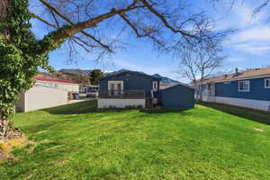 Rear view of property featuring a lawn, a deck with mountain view, a storage shed, and french doors