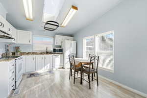 Kitchen featuring white appliances, white cabinets, light wood-type flooring, lofted ceiling, and ornamental molding