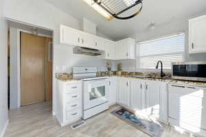 Kitchen with white appliances, white cabinetry, crown molding, light wood-type flooring, and lofted ceiling