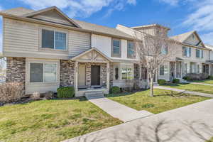View of front of property with stone siding, a front yard, and roof with shingles