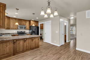 Kitchen featuring wood finish cabinets, stainless steel appliances, a chandelier, new wood-style flooring, and a peninsula