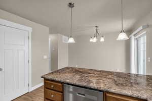 Kitchen featuring dishwasher, dark stone counters, decorative light fixtures, light wood finished floors, and wood finish cabinets