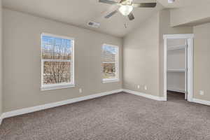 Master with a walk in closet, carpet floors, ceiling fan, and vaulted ceiling