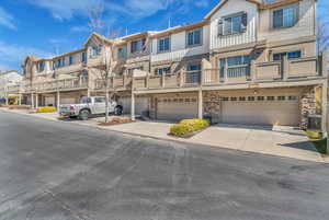 View of rear facade with driveway, attached 2-car garage, stone siding, a balcony, and a residential view