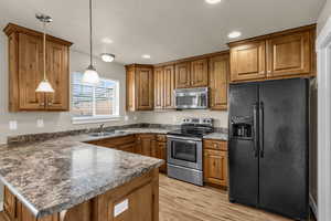 Kitchen with wood finish cabinets, stainless steel appliances, a peninsula, dark countertops, and decorative light fixtures
